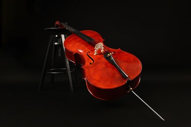 Photo of Beautiful cello and stool on black background. Classic musical instrument