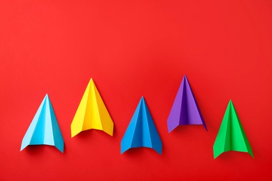 Photo of Colorful paper planes on red background, top view