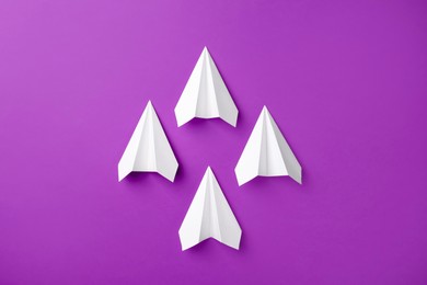 White paper planes on purple background, top view