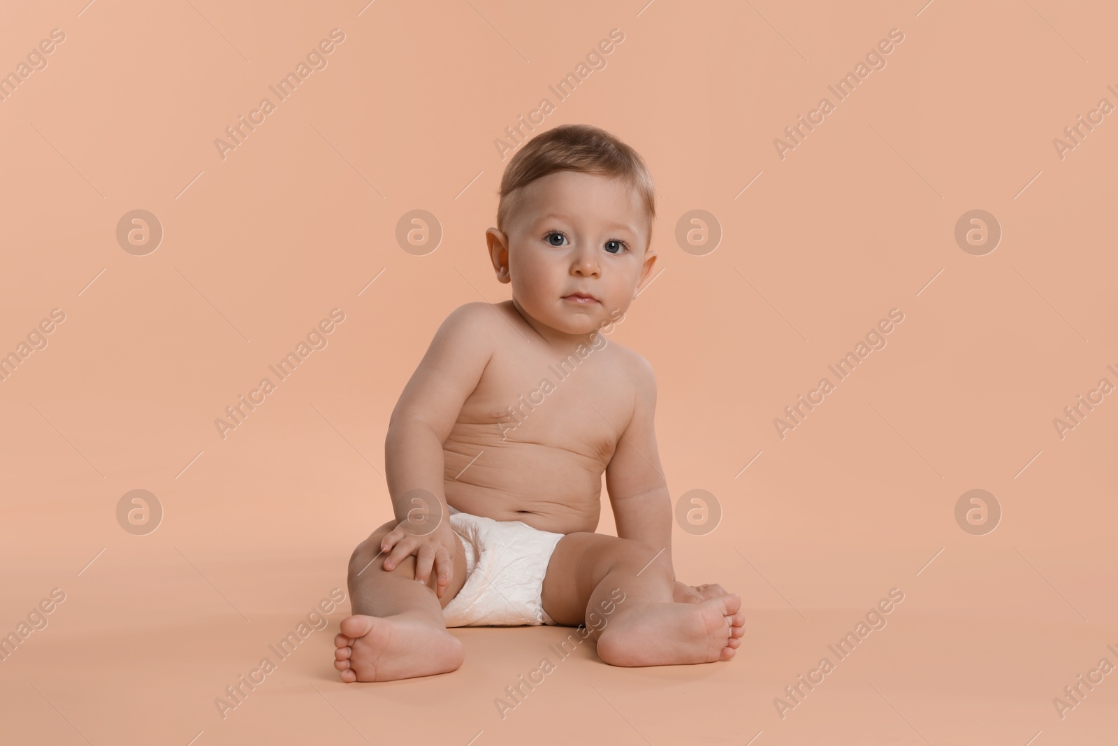 Photo of Cute little baby in diaper sitting on beige background