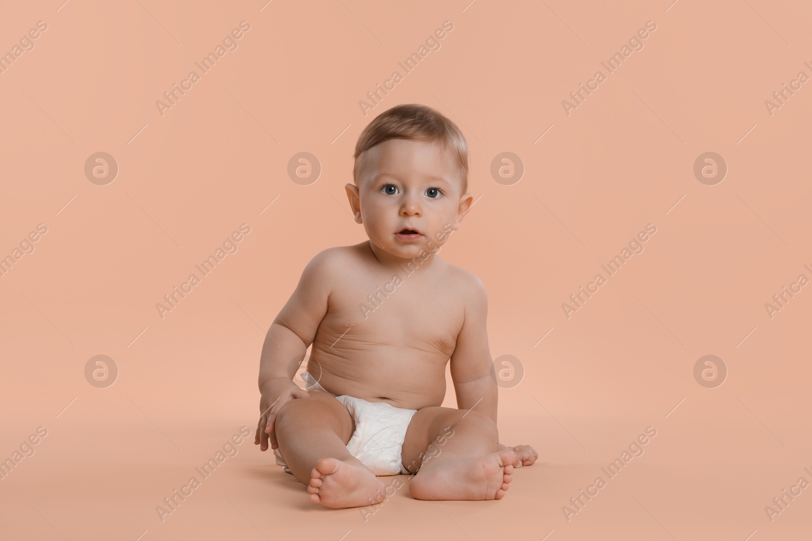 Photo of Cute little baby in diaper sitting on beige background