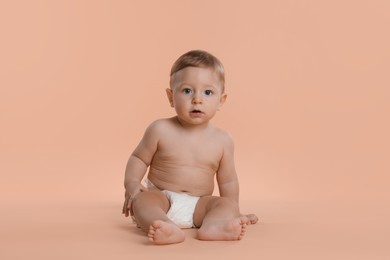 Photo of Cute little baby in diaper sitting on beige background