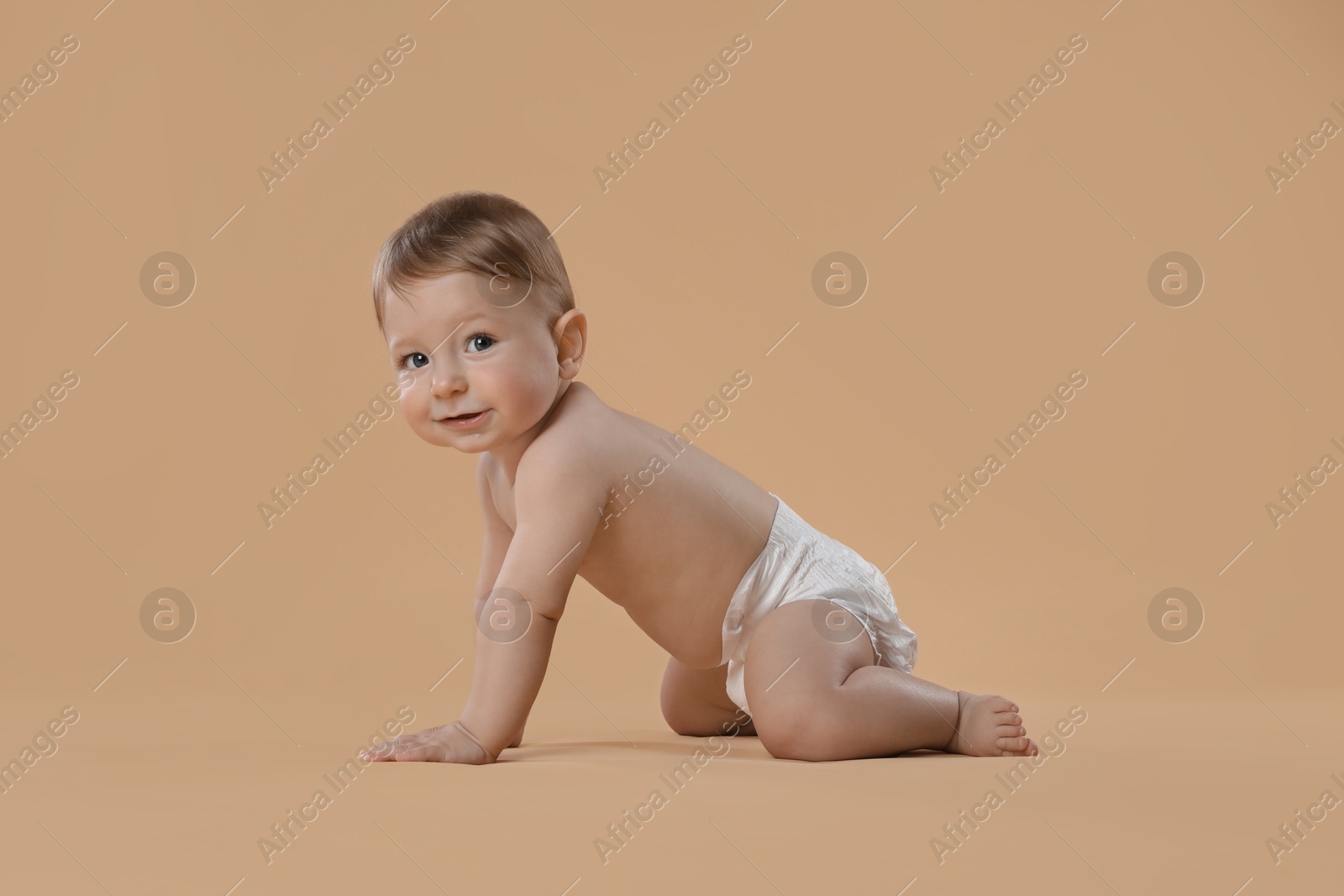 Photo of Cute little baby in diaper crawling on beige background