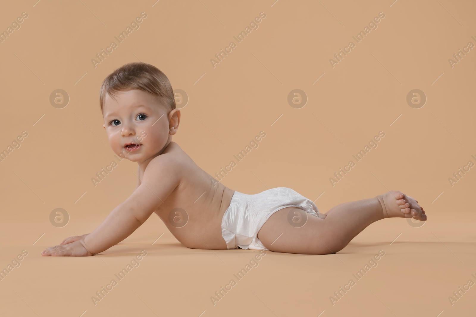 Photo of Cute little baby in diaper crawling on beige background