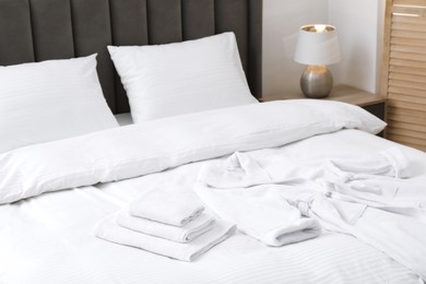 Photo of Comfortable bed with clean linens, pillows, towels and bathrobe indoors