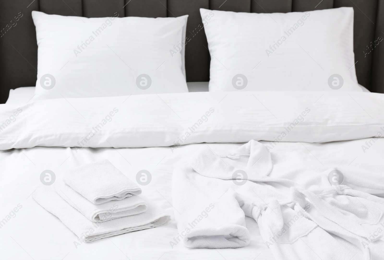 Photo of Comfortable bed with clean linens, pillows, towels and bathrobe indoors