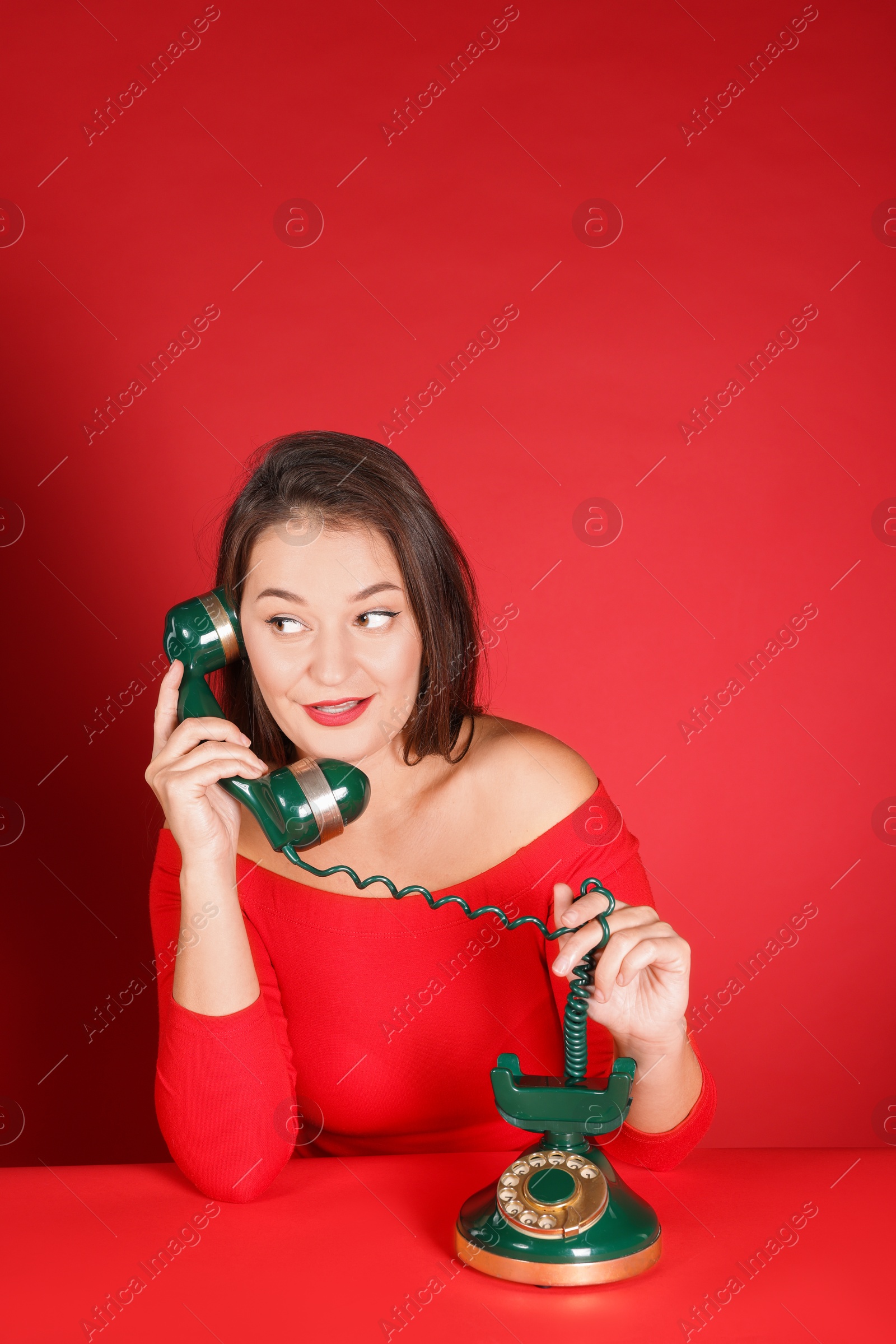 Photo of Woman talking on green vintage telephone against red background