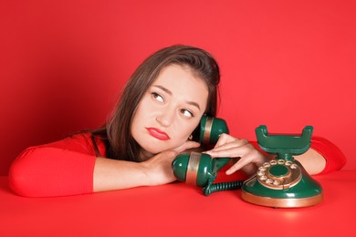 Photo of Sad woman talking on green vintage telephone against red background