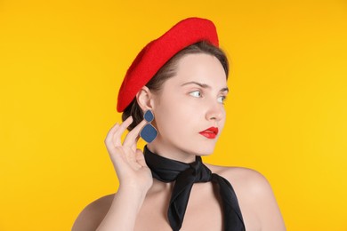 Photo of Beautiful young woman with red beret and black neckerchief on yellow background