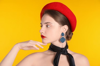 Photo of Beautiful young woman with red beret and black neckerchief on yellow background