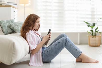 Photo of Beautiful teenage girl using smartphone on floor at home