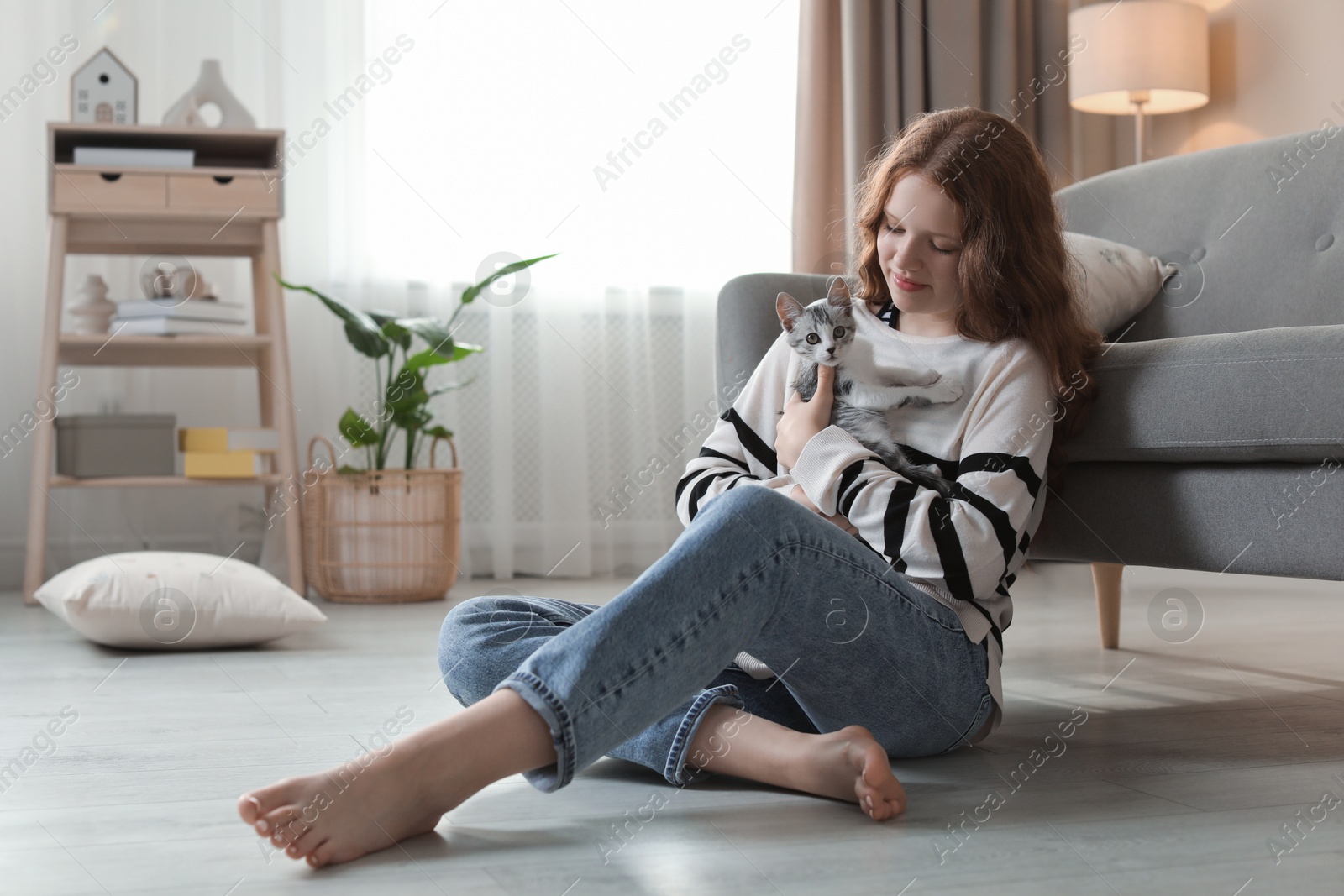 Photo of Beautiful teenage girl with cute cat on floor at home