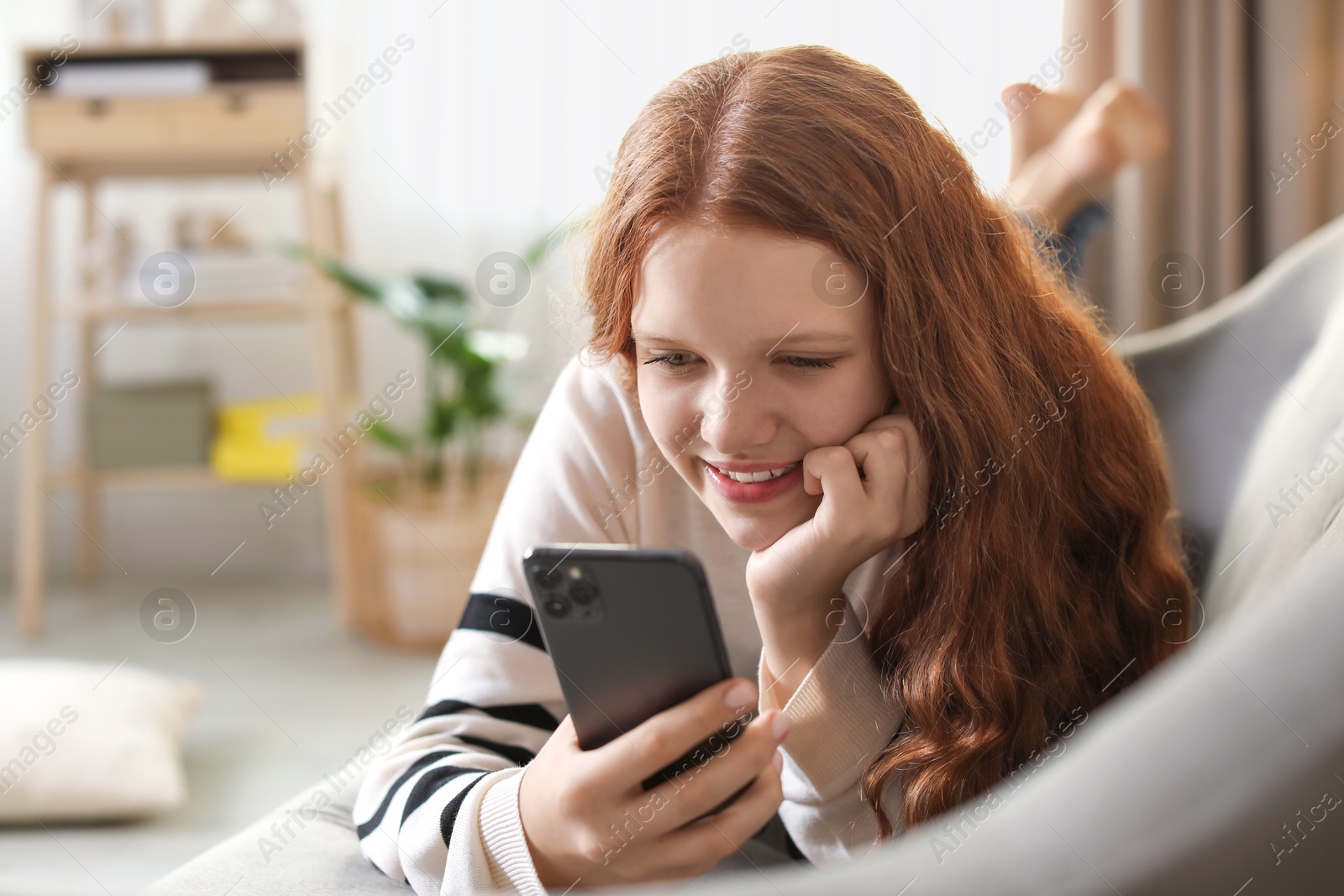 Photo of Beautiful teenage girl using smartphone on sofa at home