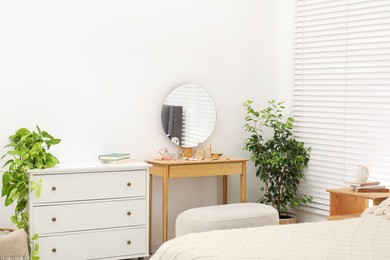 Photo of Mirror, dressing table, houseplants, bed and chest of drawers indoors. Interior design