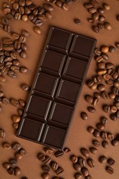 Photo of Tasty chocolate bar and coffee beans on brown background, flat lay