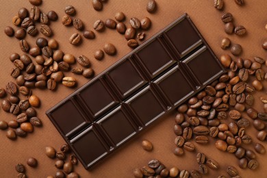 Tasty chocolate bar and coffee beans on brown background, flat lay