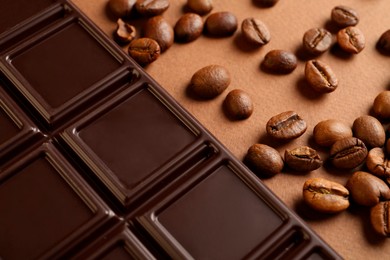 Photo of Tasty chocolate bar and coffee beans on brown background, closeup