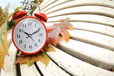 Photo of Autumn time. Alarm clock and fallen leaves on bench in park, wide angle lens