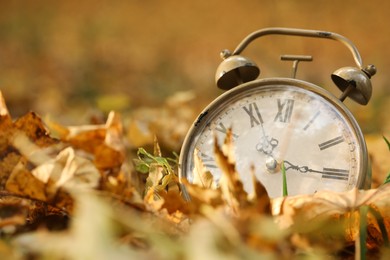 Photo of Autumn time. Vintage clock on fallen leaves in park, closeup with space for text