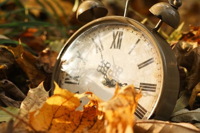 Photo of Autumn time. Vintage clock on fallen leaves in park, closeup