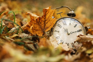 Photo of Autumn time. Vintage clock on fallen leaves in park, closeup with space for text