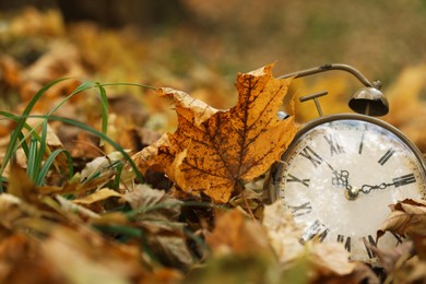 Photo of Autumn time. Vintage clock on fallen leaves in park, closeup with space for text