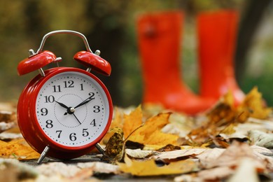 Autumn time. Alarm clock and rainboots in park, selective focus