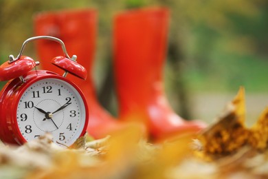 Photo of Autumn time. Alarm clock and rainboots in park, selective focus