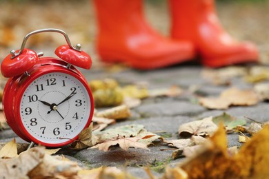 Photo of Autumn time. Alarm clock and rainboots in park, selective focus