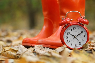 Photo of Autumn time. Alarm clock and rainboots in park