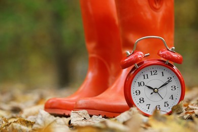 Photo of Autumn time. Alarm clock and rainboots in park