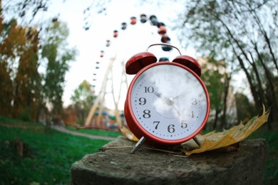 Photo of Autumn time. Alarm clock on stone in amusement park, wide angle lens