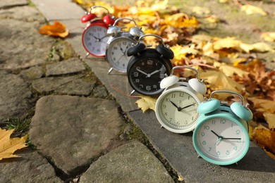 Alarm clocks on paved pathway in park at autumn, space for text