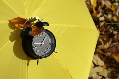 Photo of Alarm clock and yellow umbrella on dry leaves in park, closeup. Space for text