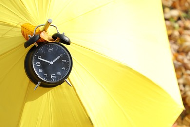 Photo of Alarm clock and yellow umbrella on dry leaves in park, closeup. Space for text