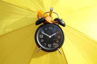 Photo of Alarm clock and yellow umbrella with dry leaves, closeup