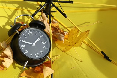 Photo of Alarm clock and dry leaves on yellow umbrella, closeup. Space for text