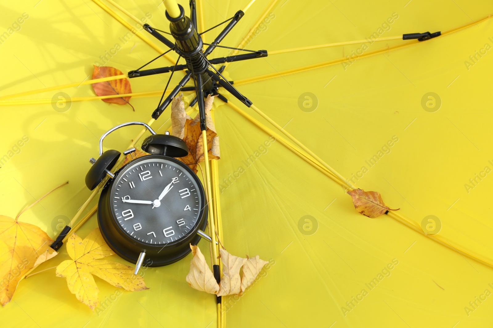 Photo of Alarm clock and dry leaves on yellow umbrella, closeup. Space for text