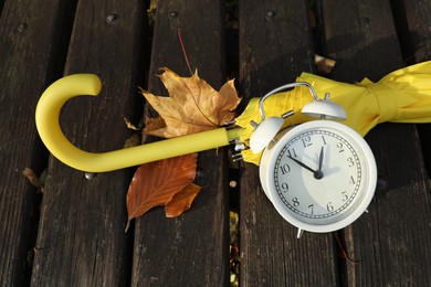 Photo of Alarm clock and yellow umbrella on wooden bench outdoors