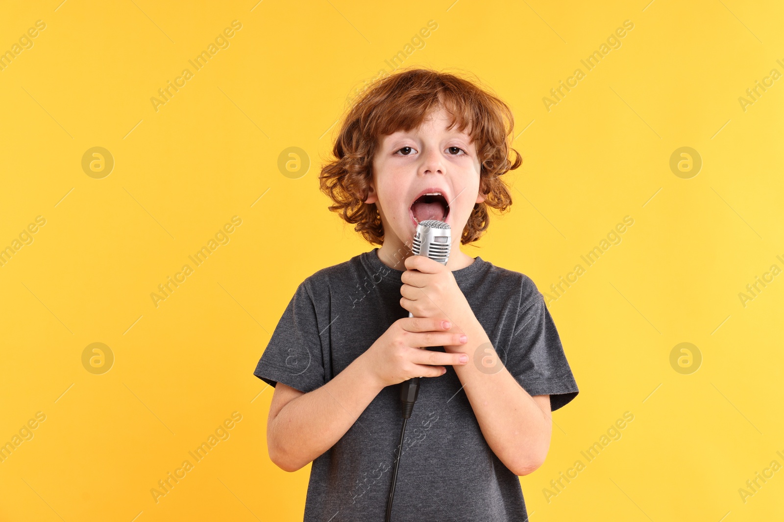 Photo of Little boy with microphone singing on yellow background