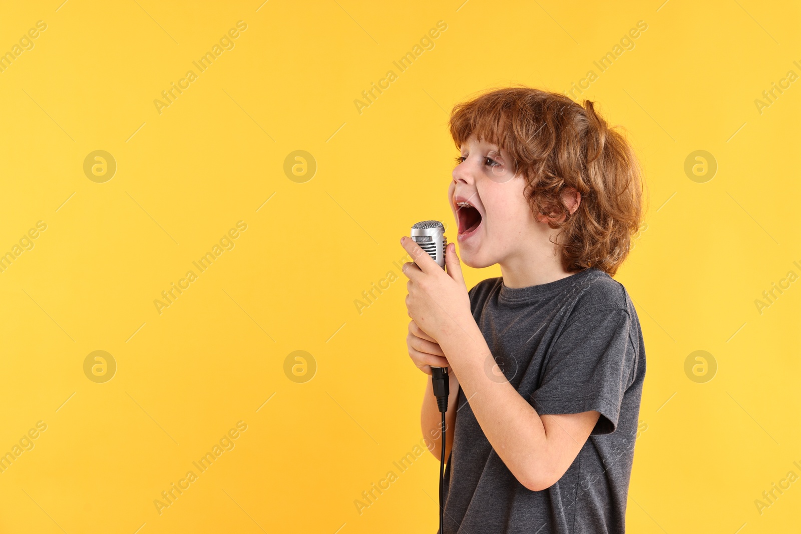 Photo of Little boy with microphone singing on yellow background, space for text