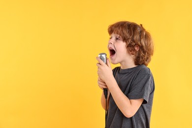 Little boy with microphone singing on yellow background, space for text