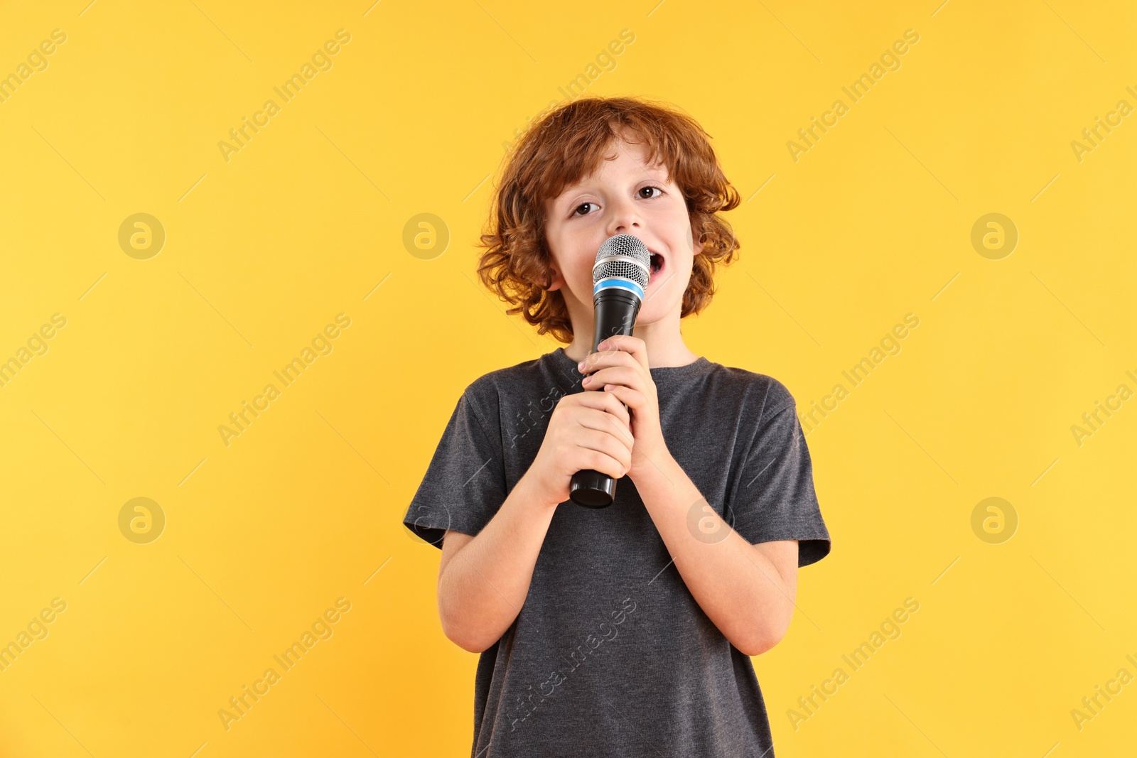 Photo of Little boy with microphone singing on yellow background