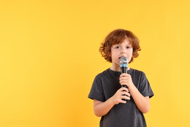 Photo of Little boy with microphone singing on yellow background, space for text