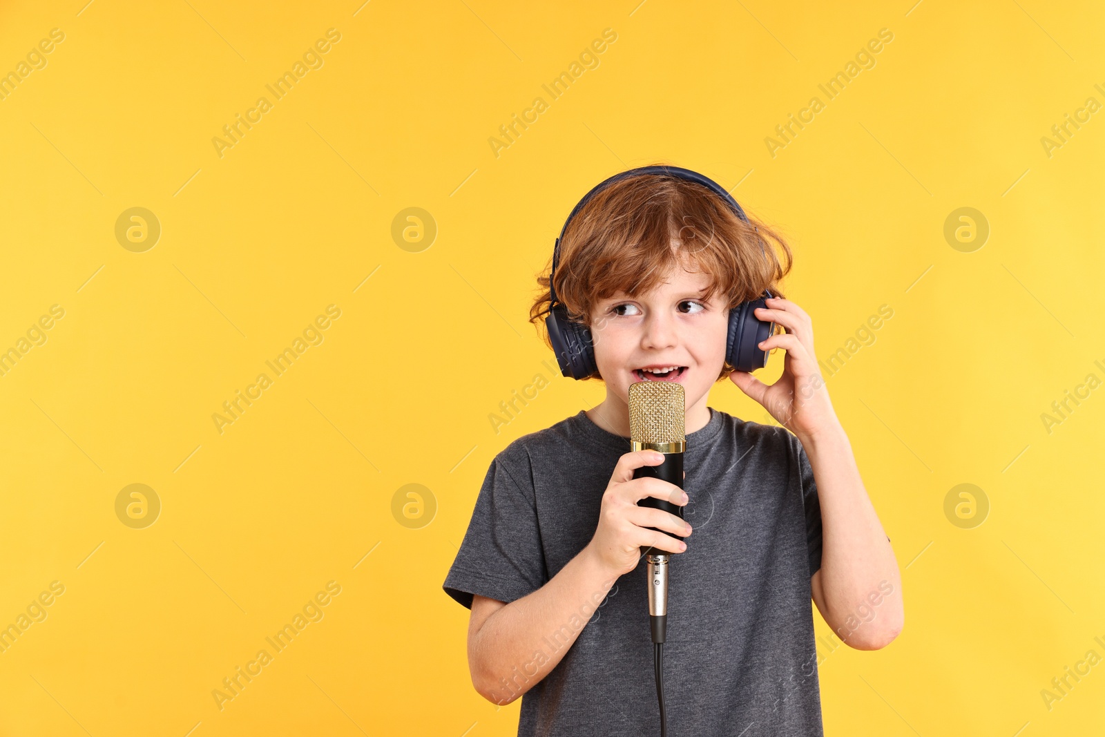 Photo of Little boy with microphone and headphones singing on yellow background, space for text