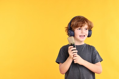 Photo of Little boy with microphone and headphones on yellow background, space for text