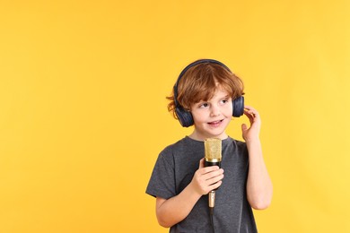 Photo of Little boy with microphone and headphones on yellow background, space for text