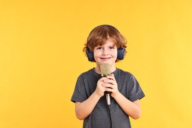 Photo of Little boy with microphone and headphones on yellow background