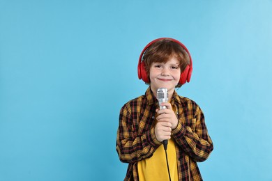 Photo of Little boy with microphone and headphones on light blue background, space for text