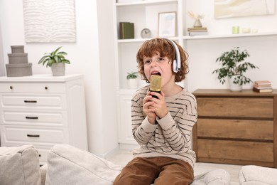 Photo of Little boy with microphone and headphones singing on sofa at home